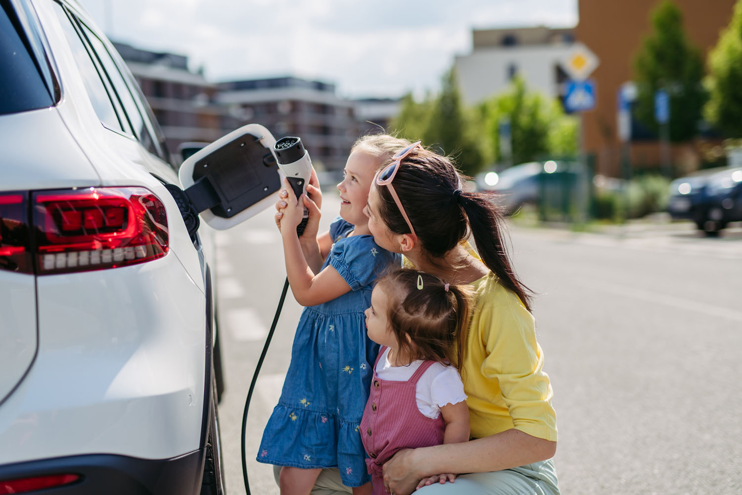 Mother and her daughters charging their electric car on the street.