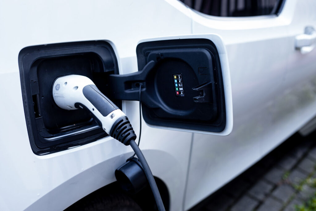 Photo of electric vehicle with power plug inserted during charging session at service station