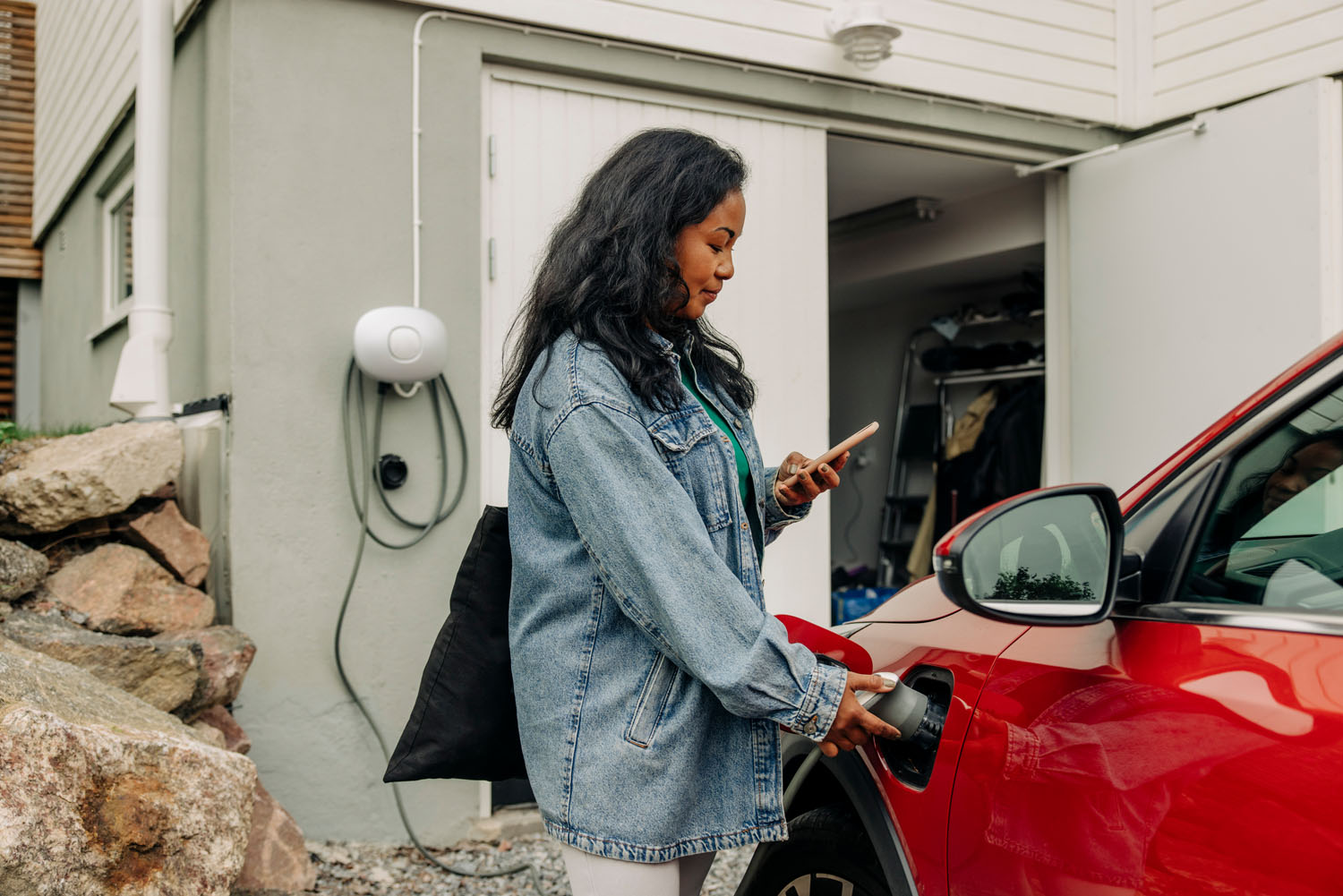 Side view of mature woman using smart phone while charging electric car
