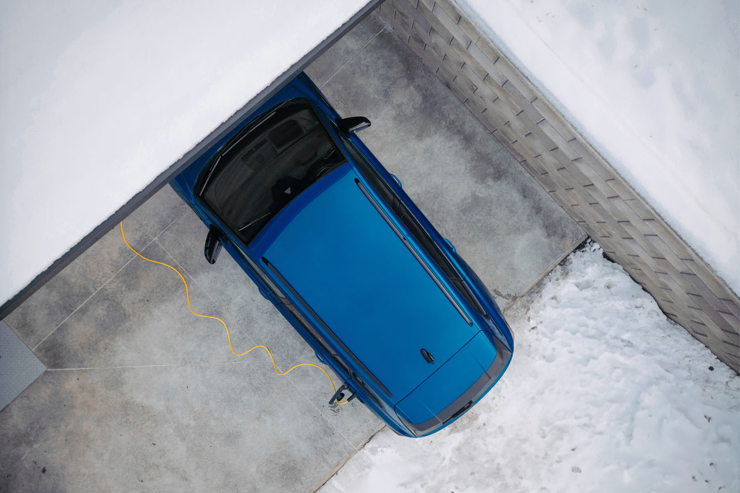 Aerial view of electric vehicle with charger in charging port during winter, cold weather.